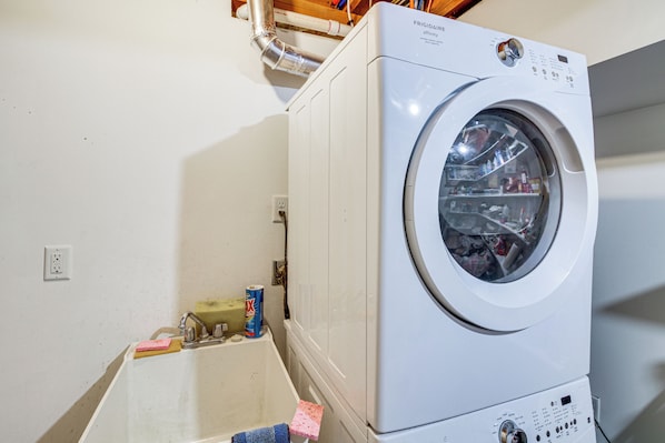 Une machine à laver à chargement frontal dans une buanderie, avec un évier et des produits de nettoyage.