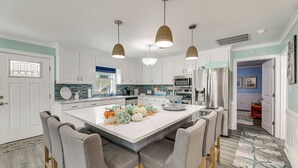 Une cuisine moderne avec des meubles blancs, un grand îlot central doté de tabourets, des luminaires suspendus et un élément décoratif central.