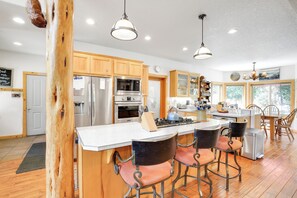 A modern kitchen with wooden cabinets, stainless steel appliances, a central island with bar stools, and pendant lighting. - Peaceful Rhododendron Cabin w/ Fire Pit & Hot Tub! (Rhododendron)