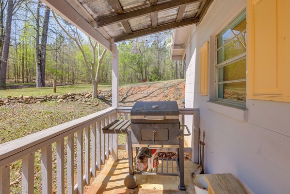 A covered porch with a grill, a wooden bench, and a view of a forested area. - Lake Gerald Cabin Rental w/ Boat Dock & Grill! (Delta)