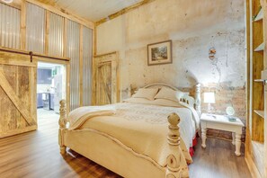 A bedroom with a wooden bed, a nightstand, and a brick wall. - Downtown Lineville Vacation Rental ~ 10 Mi to Lake (Lineville)