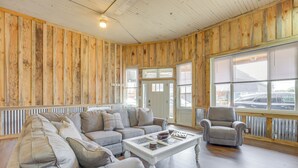 A room with a wooden paneled wall, a grey sectional sofa, a white coffee table, and a grey armchair.