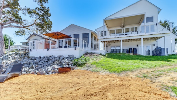 A two-story beachfront house with a covered patio, a large deck, and a sandy beach area with lounge chairs. - White Sail on the Potomac - Coastal Modern (Colonial Beach)