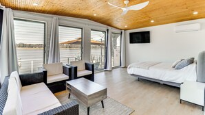 A modern room with a wooden ceiling, large windows, a bed, a sofa, and a TV. - White Sail on the Potomac - Coastal Modern (Colonial Beach)
