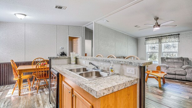 A kitchen with a granite countertop, wooden cabinets, a double sink, and a dining area with wooden chairs. - 7 Mi to Crystal River: Home w/ Yard & Fire Pit! (Citrus Springs)