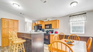 A kitchen with wooden cabinets, a central island with stools, a dining table with chairs, and a window with a valance. - 7 Mi to Crystal River: Home w/ Yard & Fire Pit! (Citrus Springs)