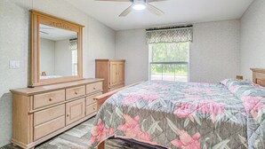 A bedroom with a bed, dresser, mirror, ceiling fan, window with curtains, and a view of greenery outside. - 7 Mi to Crystal River: Home w/ Yard & Fire Pit! (Citrus Springs)