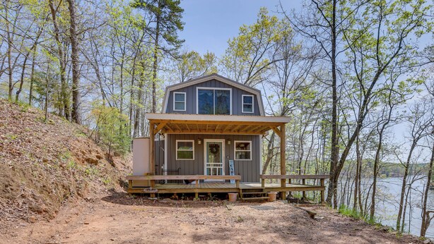 A cabin with a wooden deck, a front porch, and a view of the lake. - Lakefront Delta Cabin Rental w/ Boat Dock + Deck! (Delta)
