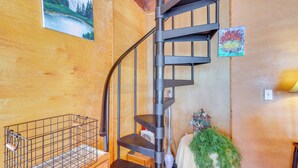 A spiral staircase with a metal railing, a wooden wall with a painting, and a small table with a decorative item. - Lakefront Delta Cabin Rental w/ Boat Dock + Deck! (Delta)