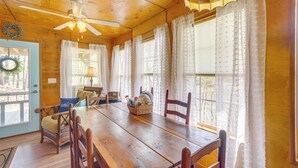 A wooden dining room with a wooden table, chairs, a ceiling fan, and a window with curtains. - Lakefront Delta Cabin Rental w/ Boat Dock + Deck! (Delta)