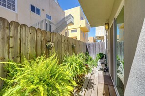 A wooden deck with ferns and a scooter, adjacent to a building with a white exterior and a window. - Sleek Oxnard Townhouse w/ Balconies: Walk to Beach (Oxnard)