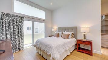 A bedroom with a large bed, a nightstand, a desk, and a view through a sliding door.