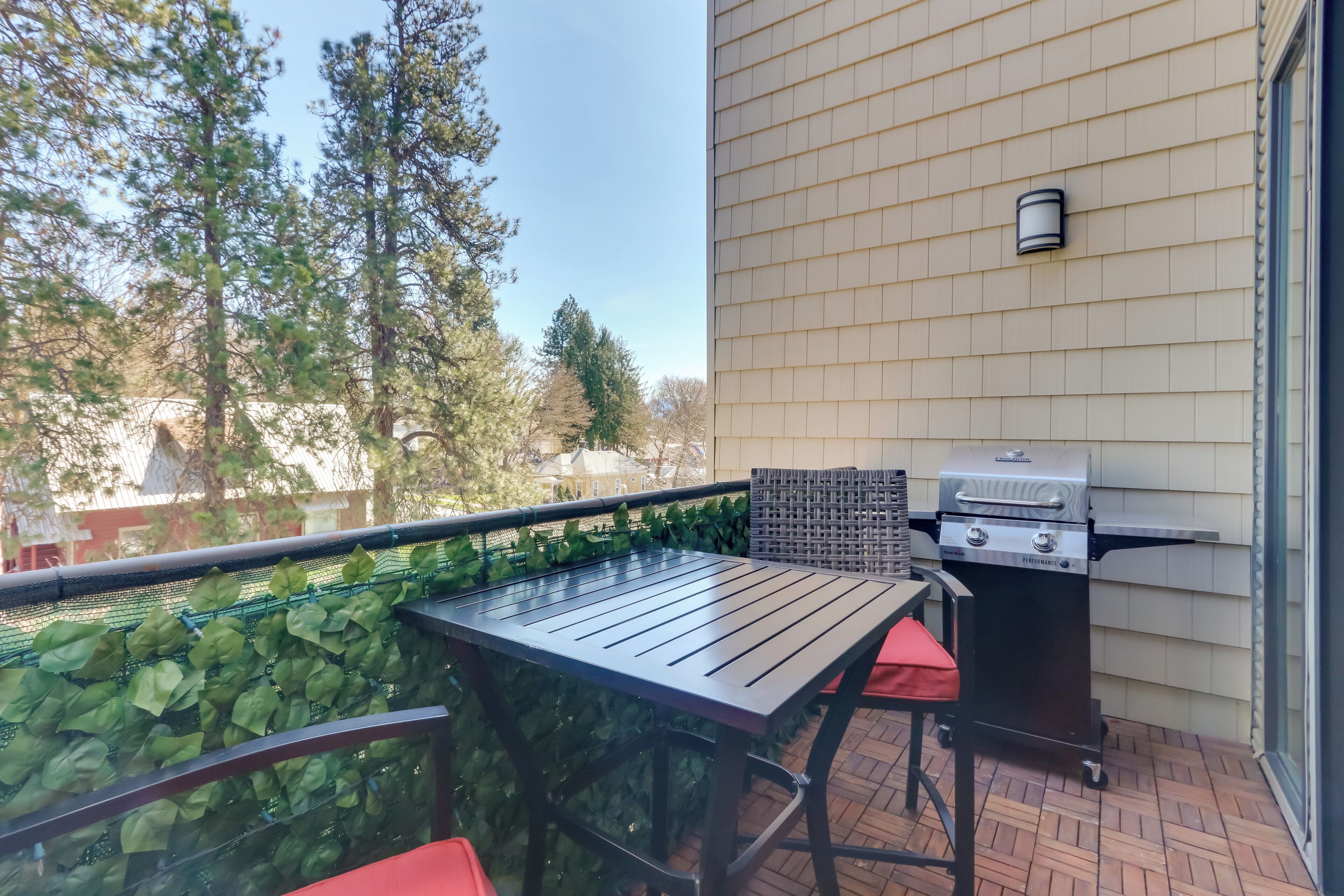 A balcony with a table and chairs, a grill, and a view of trees and buildings.