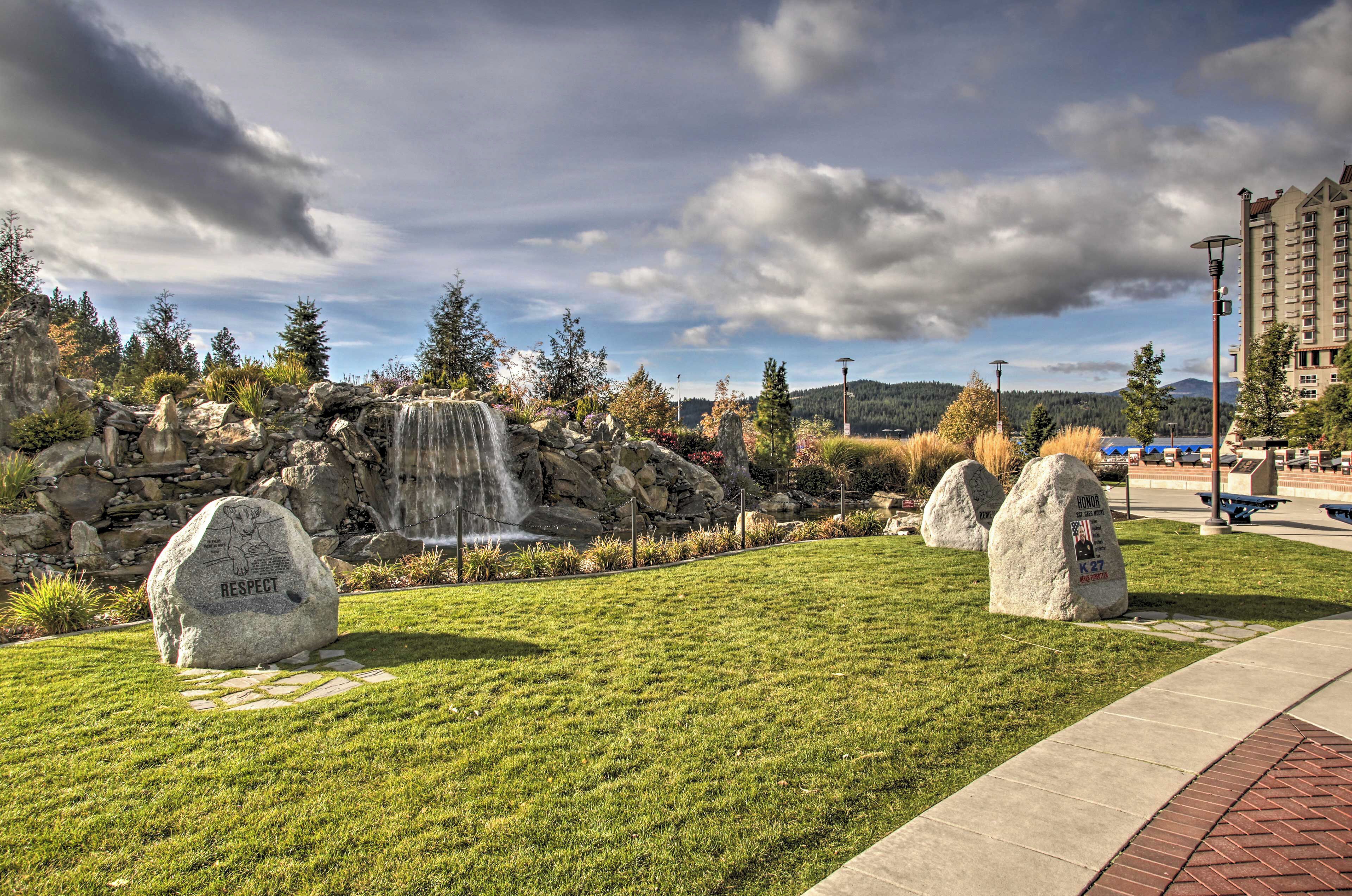 A landscaped area with a waterfall, large rocks with inscriptions, and a paved walkway.