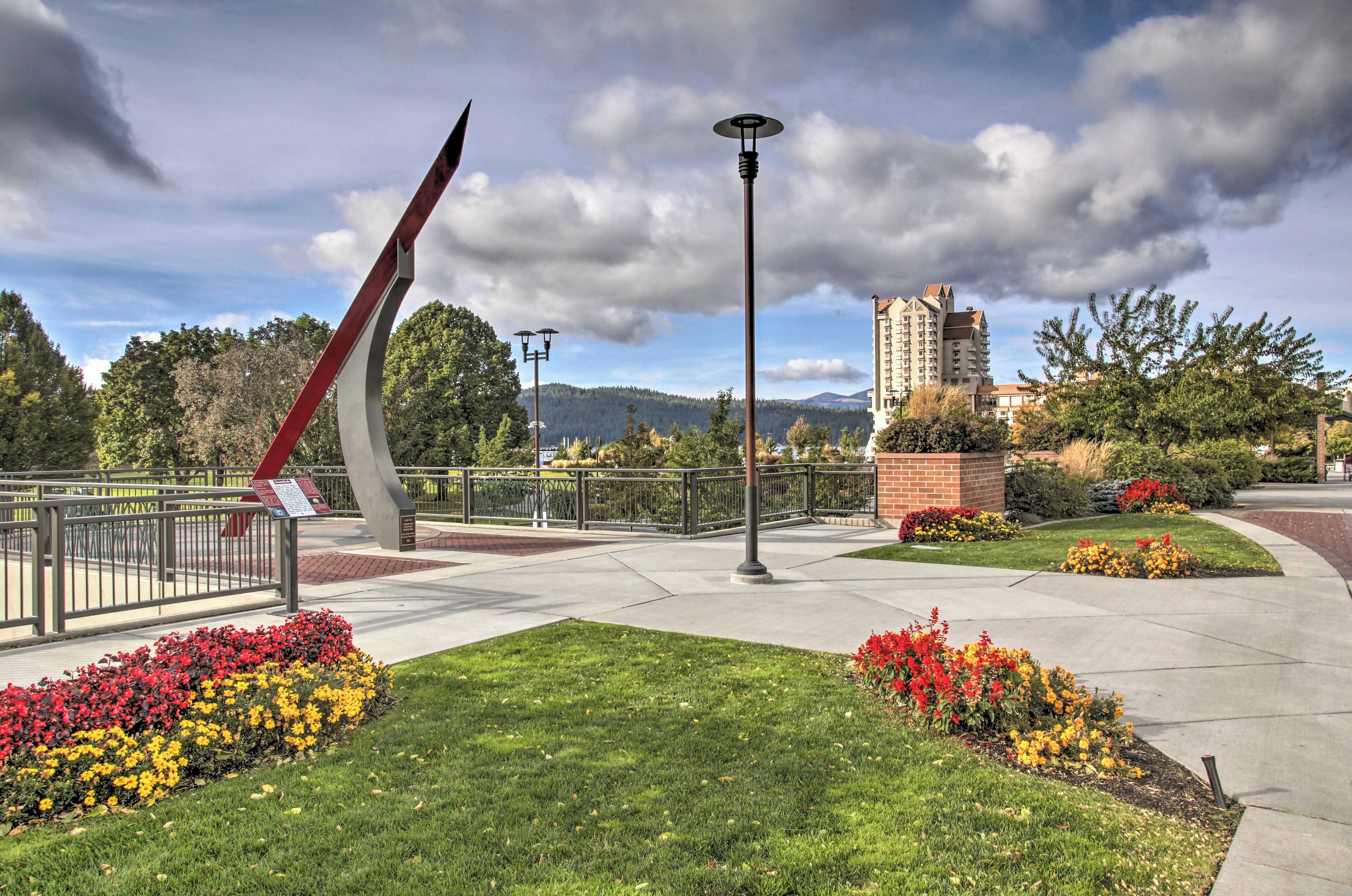 A landscaped area with a modern sculpture, a tall street lamp, and a building in the background.