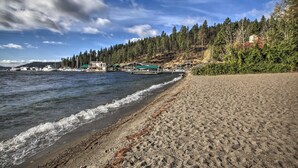 A beach with a wooden pier extending into calm waters, surrounded by dense forest and a clear sky.