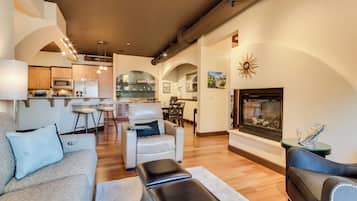 A modern living room with a sofa, ottoman, and a fireplace. There is a dining area with a table and chairs in the background.