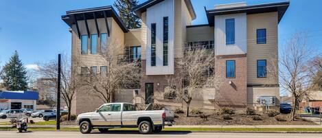 A modern multi-story building with a mix of brick and siding exterior, large windows, and a parked truck on the street.