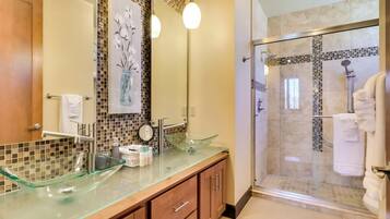 A modern bathroom with a glass vessel sink, wooden cabinets, a glass-enclosed shower, and a tiled backsplash.