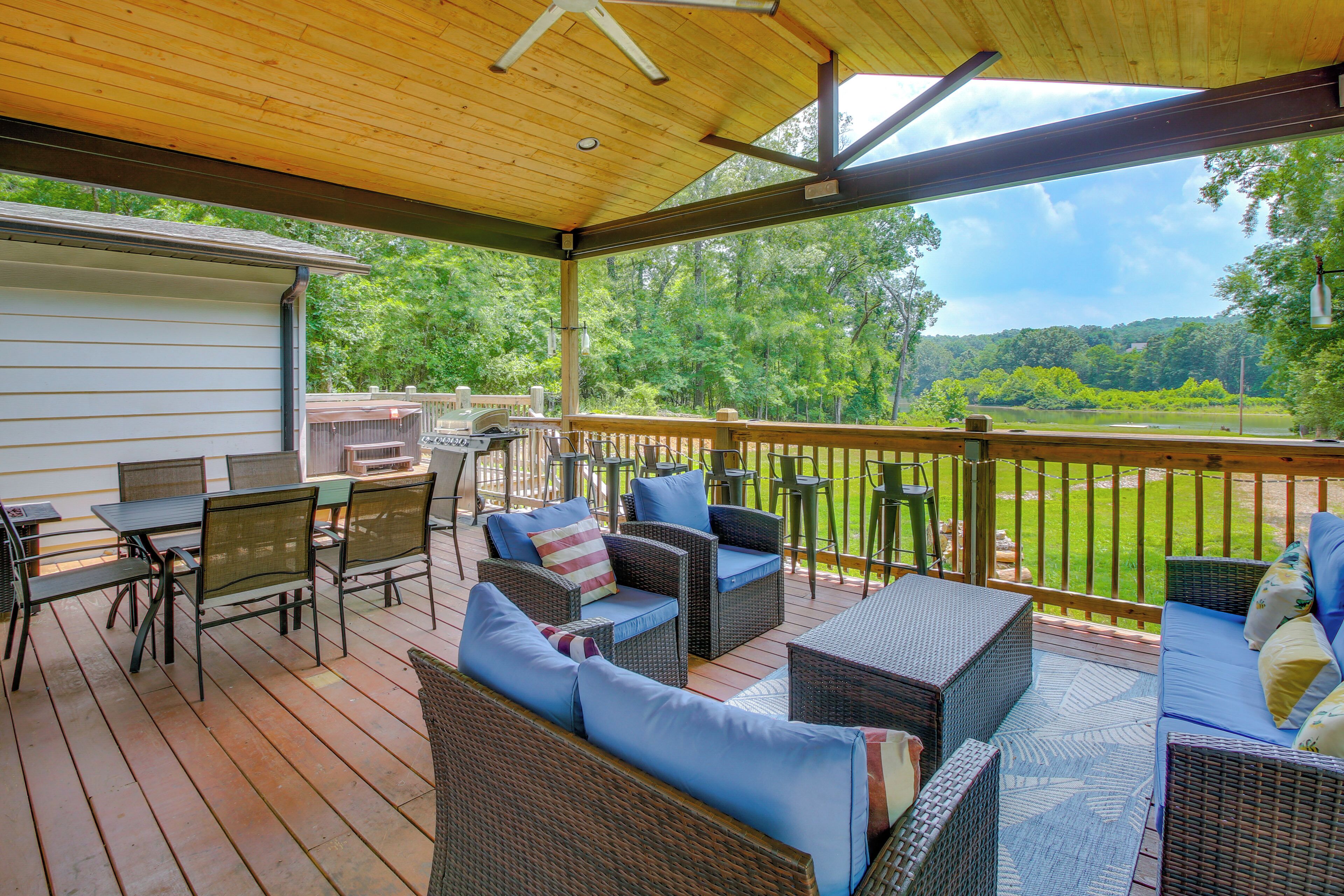 A covered outdoor deck with wicker furniture, a grill, and a view of a wooded area.