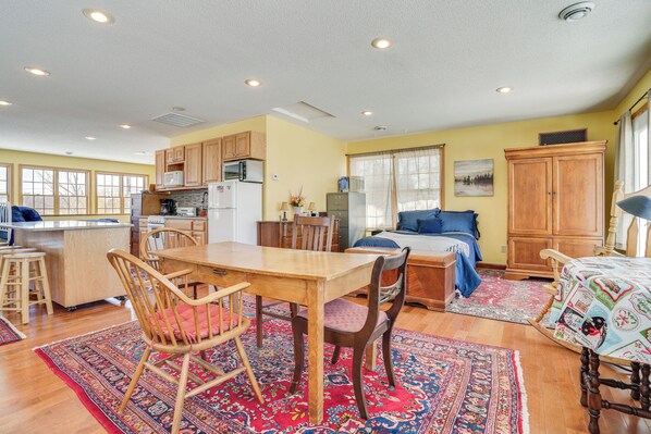A spacious living area with a wooden dining table, chairs, a sofa, and a bed. There is a kitchen area with wooden cabinets and appliances. - Waterfront Forest Lake Studio w/ Shared Dock! (Forest Lake)