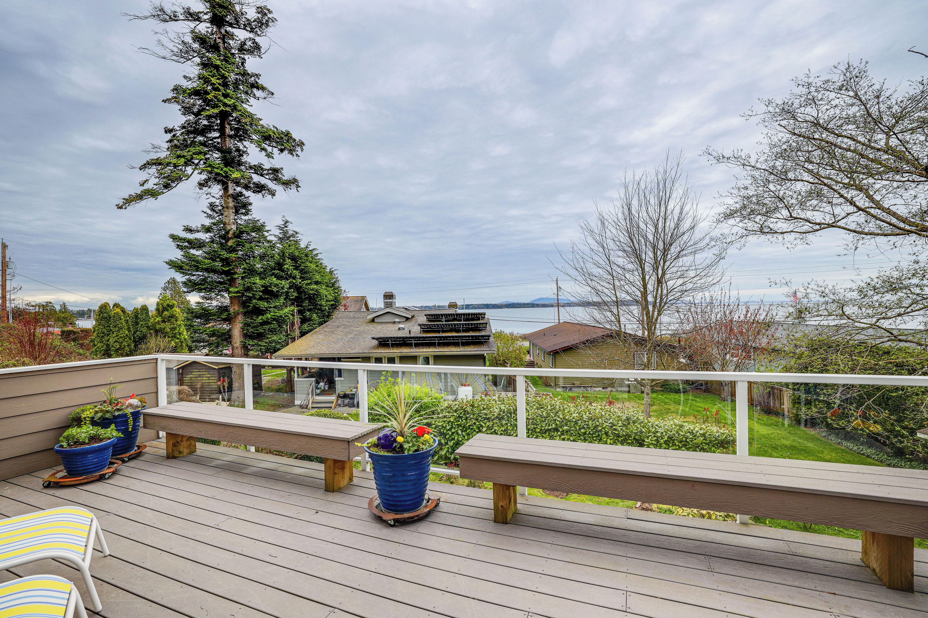 A wooden deck with benches and potted plants, overlooking a residential area with houses and trees.