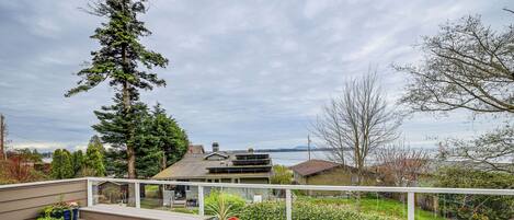 A wooden deck with benches and potted plants, overlooking a residential area with houses and trees.