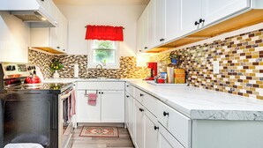 A modern kitchen with white cabinets, a tiled backsplash, and a window with a red valance. - Lakeview Vacation Rental - Walk to Crystal Lake! (Lakeview)