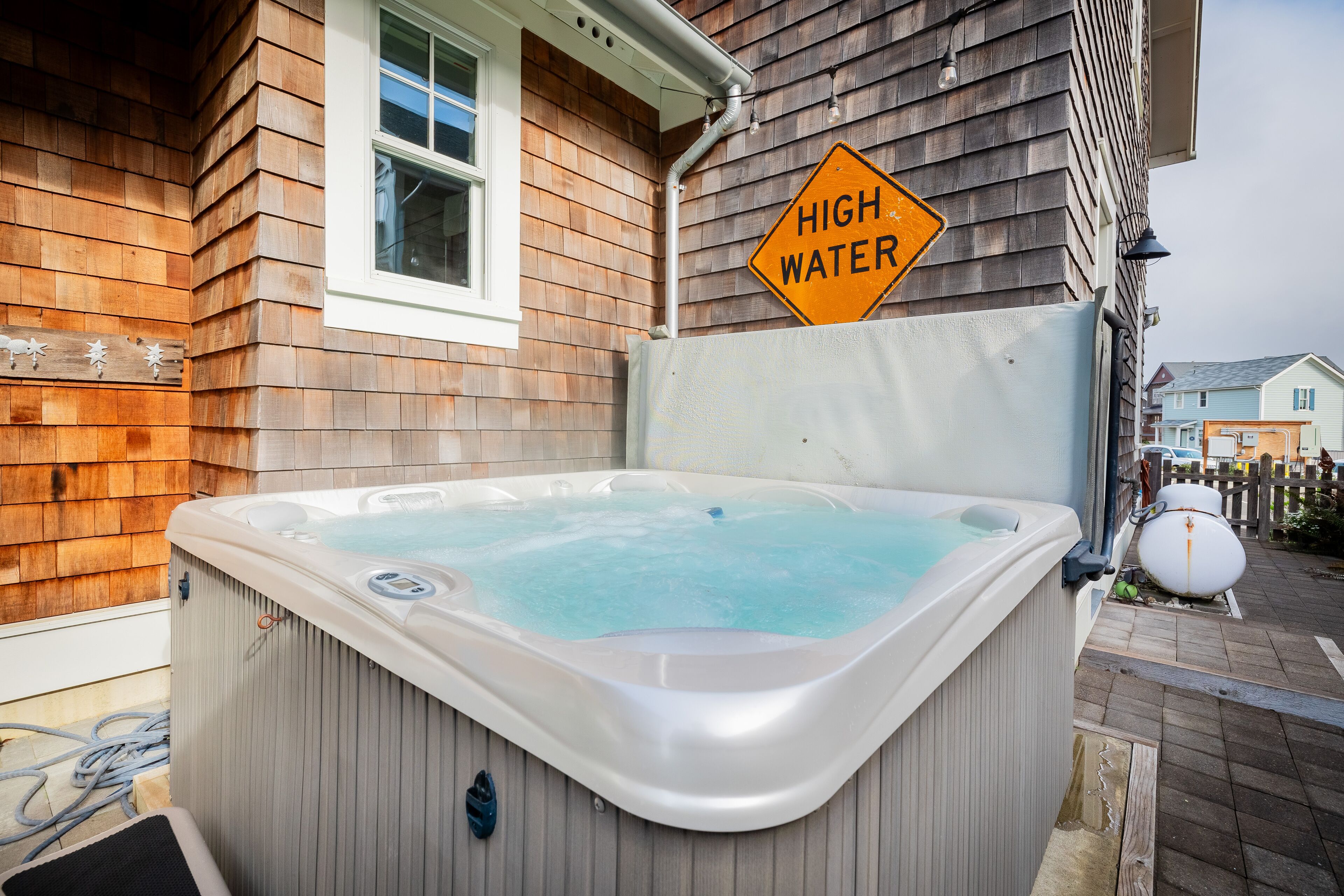 A hot tub outside a wooden house with a 'HIGH WATER' sign nearby.