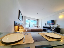 Una habitación de hotel moderna con cama, televisión y zona de comedor con platos y copas de vino.