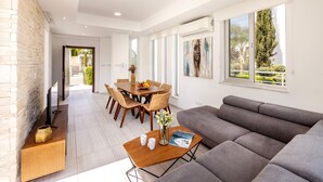 A modern living room with a grey sofa, a wooden coffee table, and a dining area with a wooden table and chairs. - 3 bedroom villa With Pool (Protaras)
