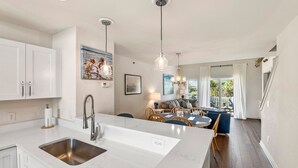 A modern kitchen with white cabinets, a stainless steel sink, and pendant lighting. - Purple Pearl: Shared Pool with Lazy River (Kill Devil Hills)