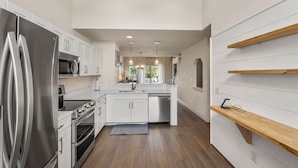 A modern kitchen with white cabinetry, stainless steel appliances, and a wooden shelf. - Purple Pearl: Shared Pool with Lazy River (Kill Devil Hills)