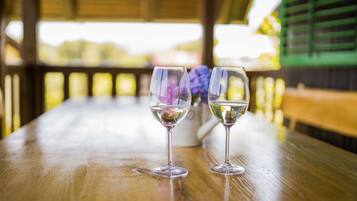 Two wine glasses on a wooden table under a covered area with a view of greenery.
