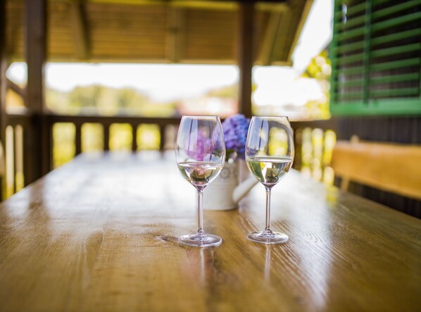Two wine glasses on a wooden table under a covered area with a view of greenery. - Holiday Home Mila (Stubicke Toplice)