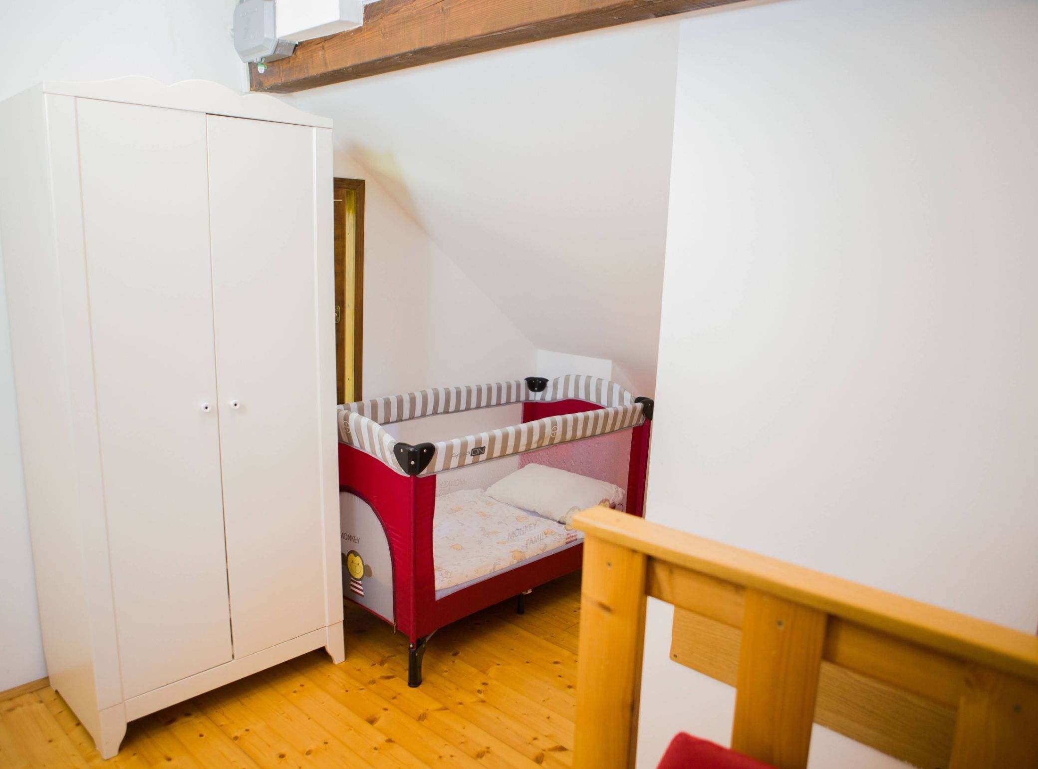 A child's bunk bed with a red frame and a white mattress, a white wardrobe, and a wooden chair.