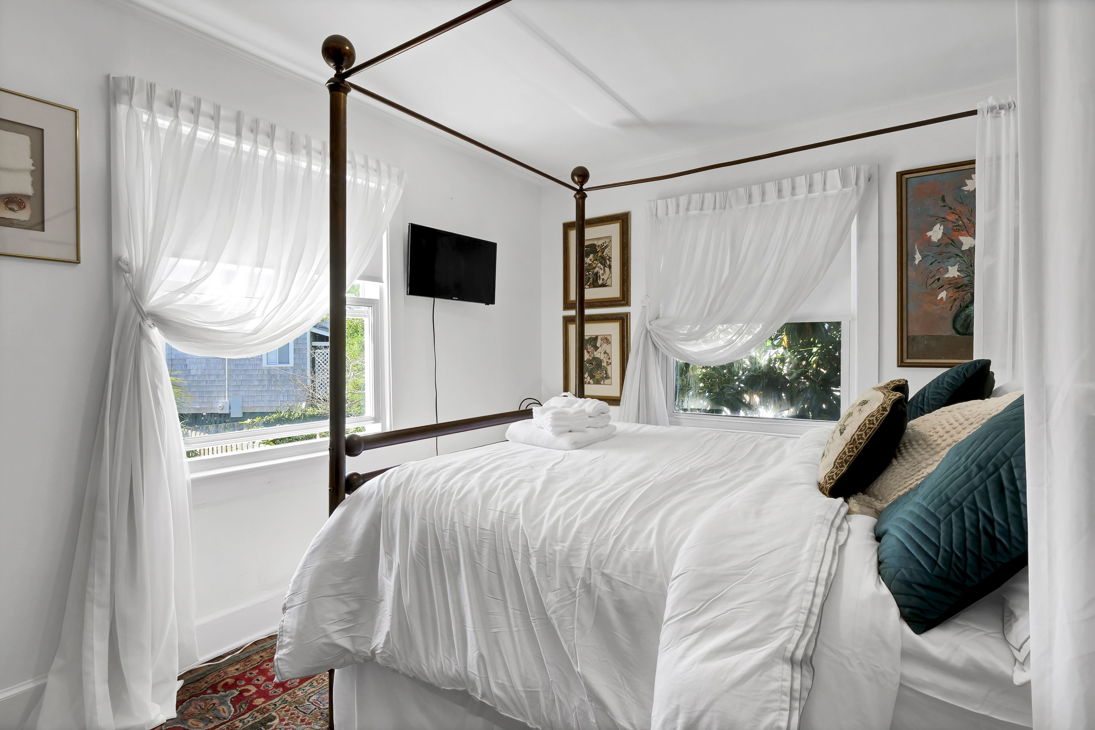 Een hemelbed met witte lakens, een flatscreen televisie aan de muur en kunstwerken erboven.