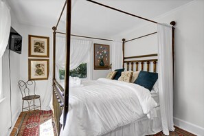 Un lit à baldaquin avec une literie blanche, un tapis rouge à motifs et une petite table avec une chaise.
