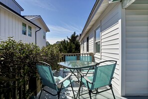 Une table à plateau en verre, entourée de quatre chaises, se trouve dans un espace patio, avec en arrière-plan des maisons au revêtement blanc.