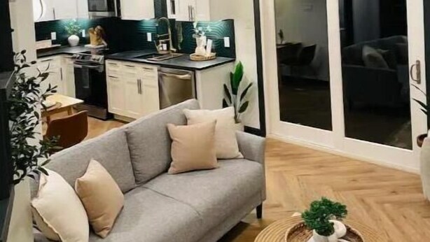 Un appartement moderne avec un canapé gris, un coin repas, une cuisine et un escalier.