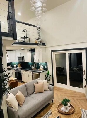 A modern apartment with a grey sofa, a dining area, a kitchen, and a staircase. - Traveler's miniBarndo Retreat, L. Greenville (Dallas)