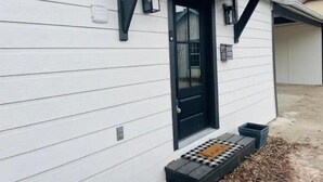 Une maison blanche avec une porte et des fenêtres noires, un petit porche avec un banc et une boîte aux lettres fixée au mur.
