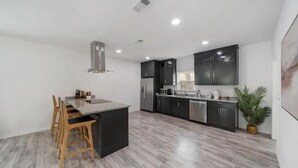 A modern kitchen with dark cabinets, a central island, and a dining area with wooden chairs.