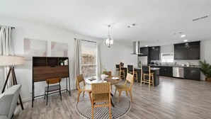 A modern kitchen with dark cabinets, a central island, and a dining area with a round table and chairs.