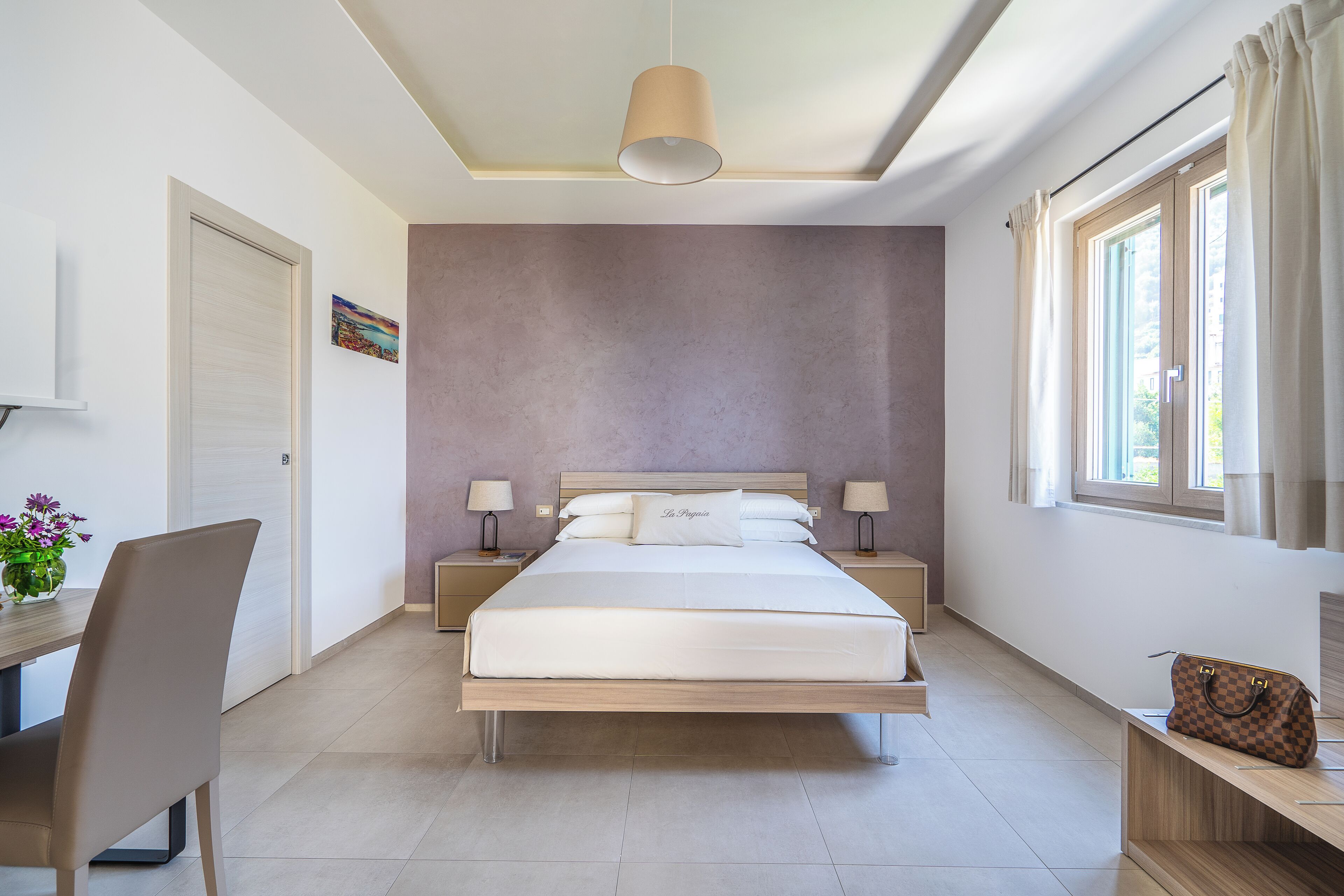 Een moderne slaapkamer met een groot bed, nachtlampjes, een bureau en een stoel.