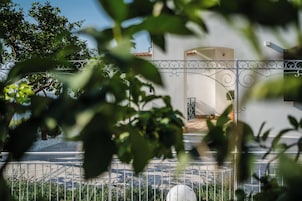 Un edificio blanco con una cerca de metal, un camino pavimentado y un árbol en primer plano.