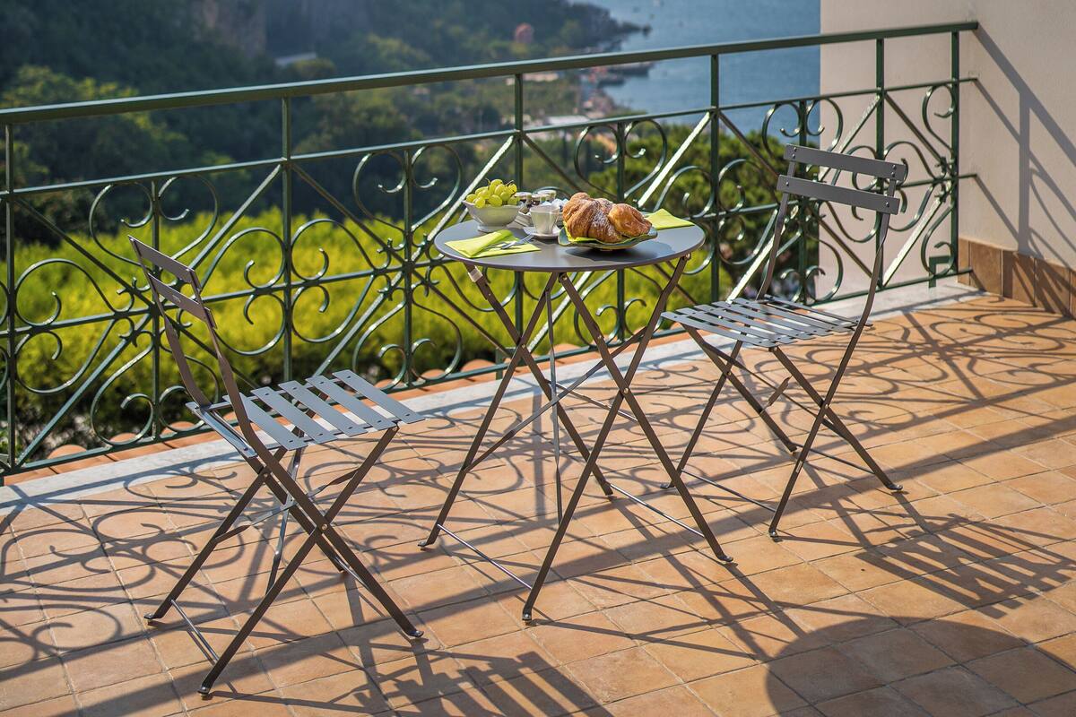 A balcony with a table and chairs, overlooking a cliff and the sea.