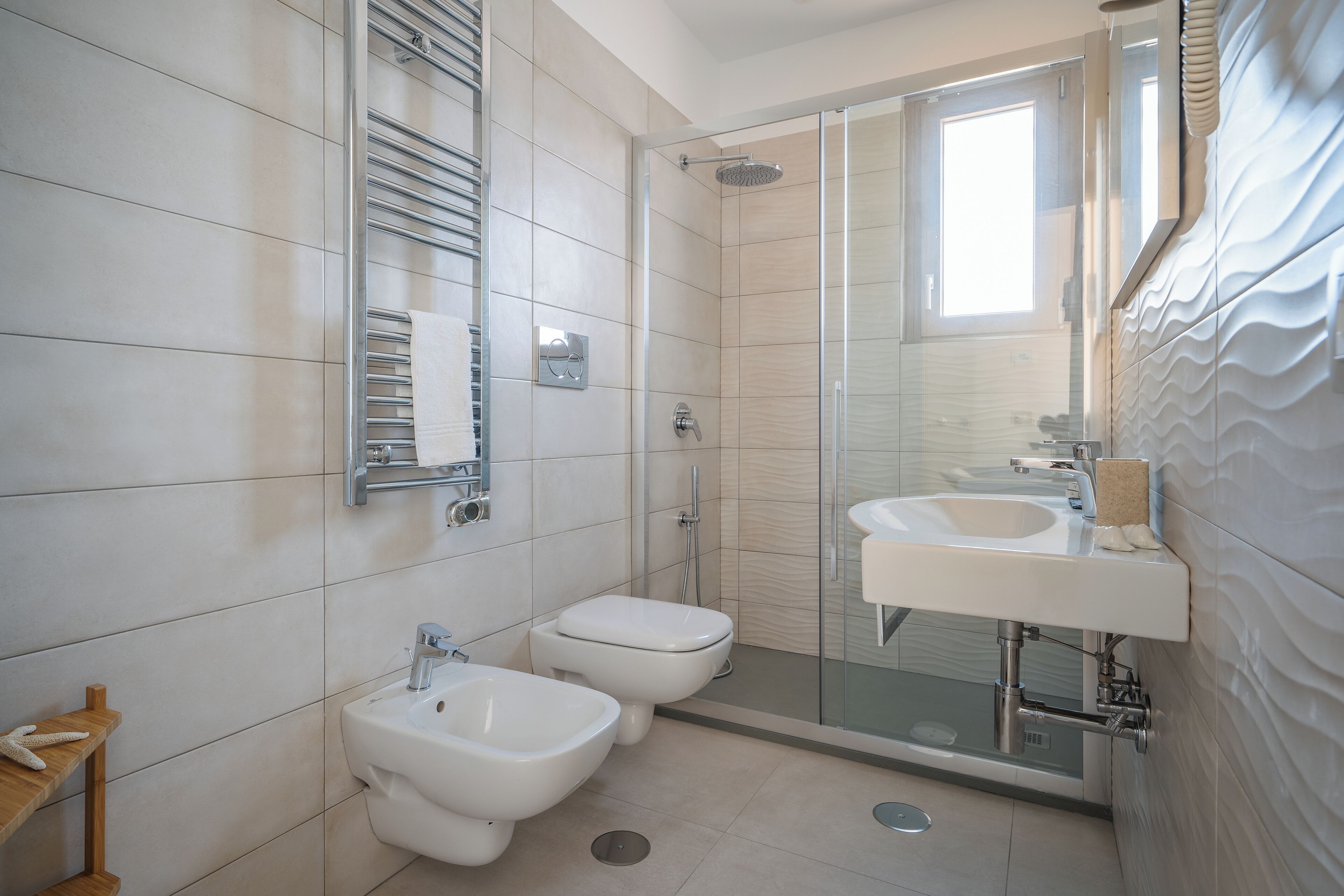 A modern bathroom with a glass shower enclosure, two sinks, and a bidet.