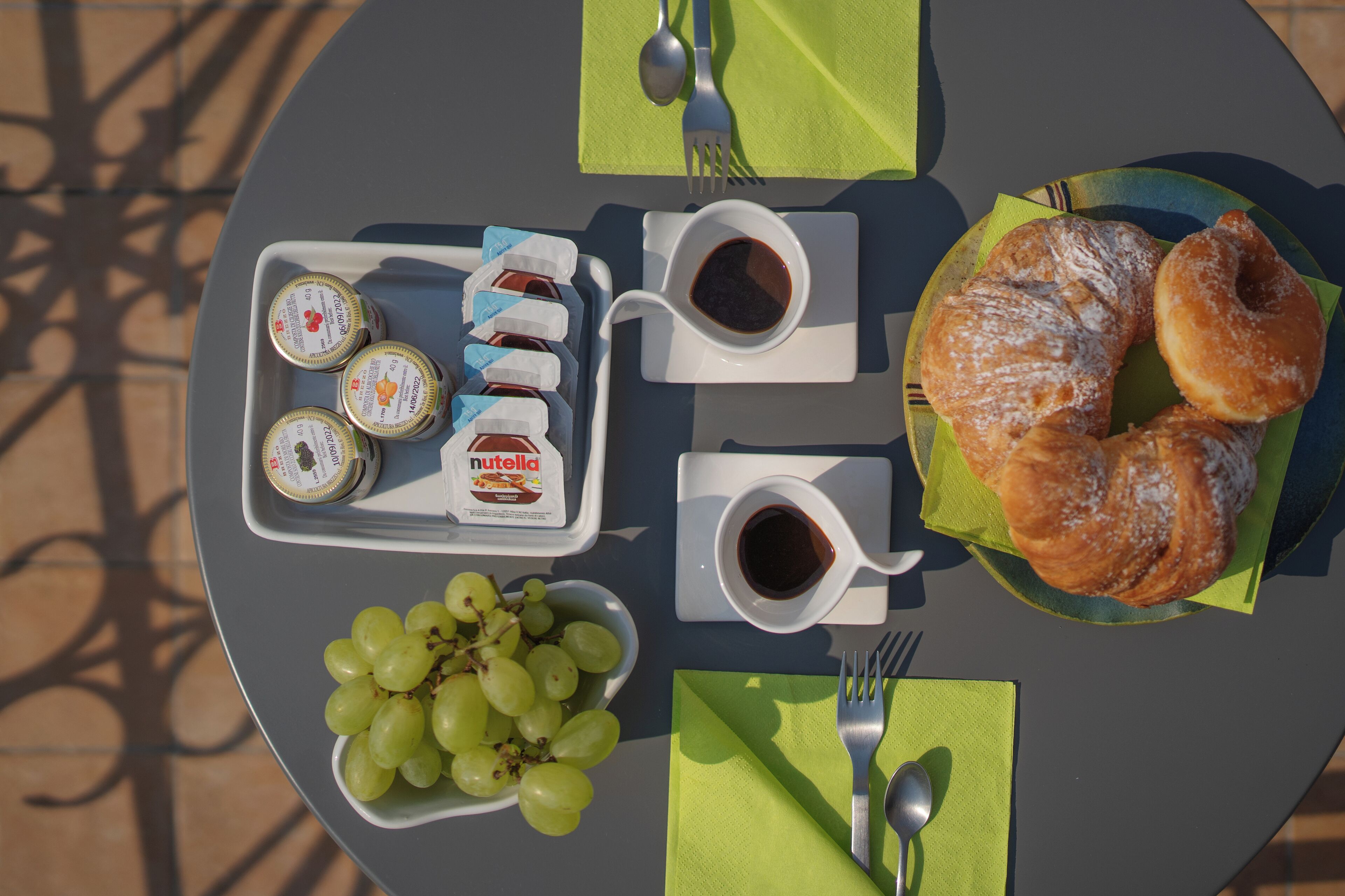 A table set with a plate of croissants, a bowl of grapes, and two cups of coffee with jam and Nutella.