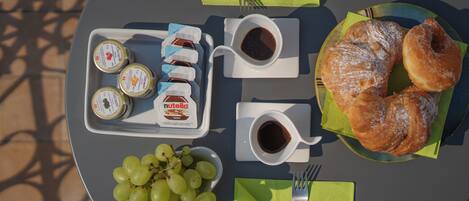 A table set with a plate of croissants, a bowl of grapes, and two cups of coffee with jam and Nutella.